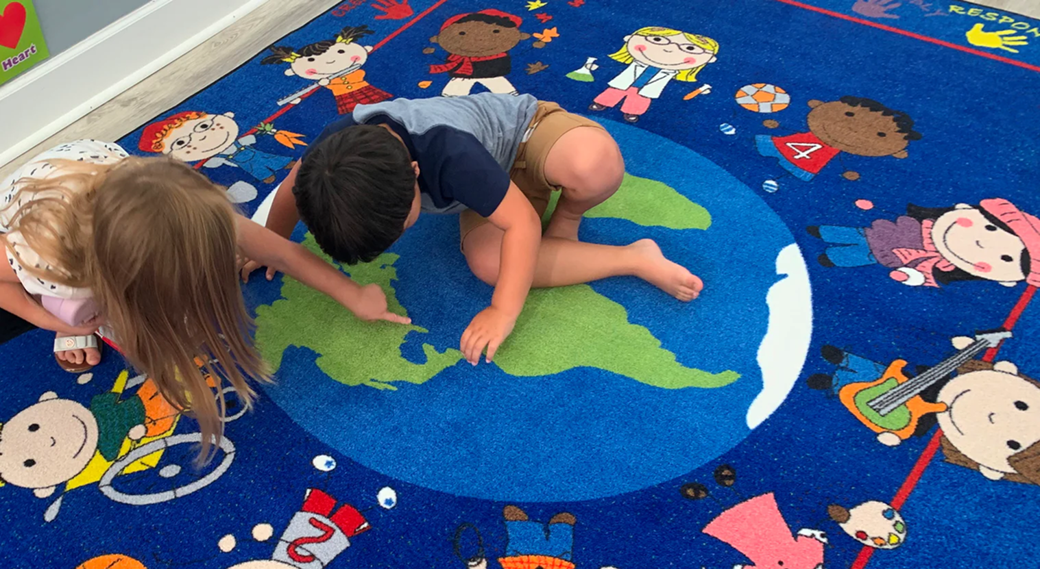 Children exploring a colorful geography rug featuring continents, countries, and oceans in a classroom, promoting hands-on learning and early geographic literacy.